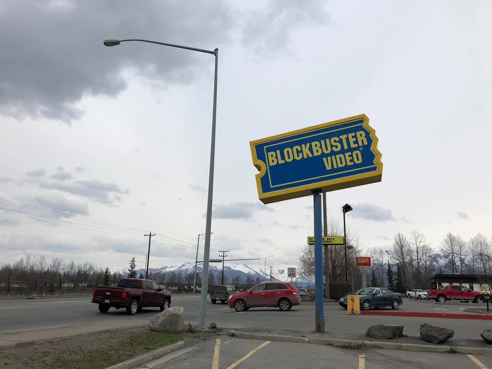 Blockbuster Video store sign standing by a road with cars driving past.