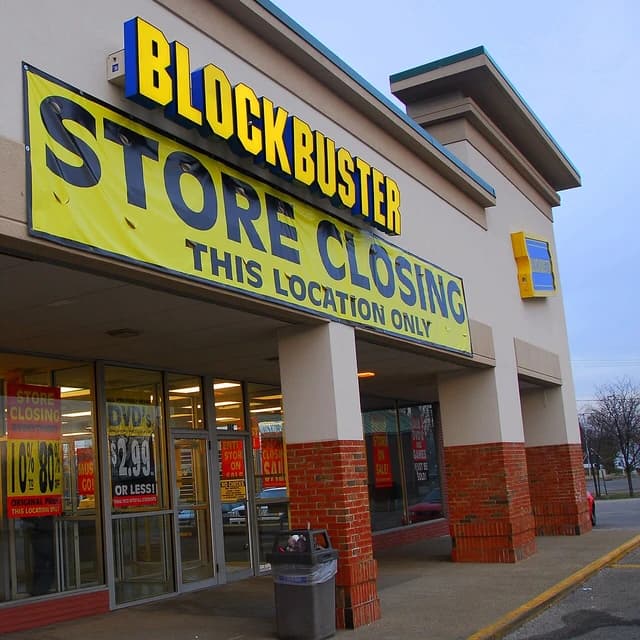 Exterior view of a Blockbuster video rental store with a large yellow 'Store Closing' banner.