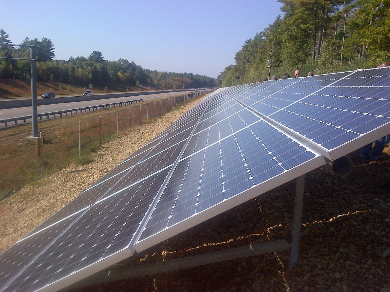 Solar array panels installed next to a highway with cars and trees in the background.