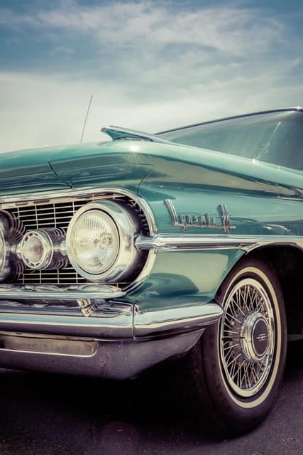 Front detail of a turquoise vintage luxury car with chrome grille and headlights.
