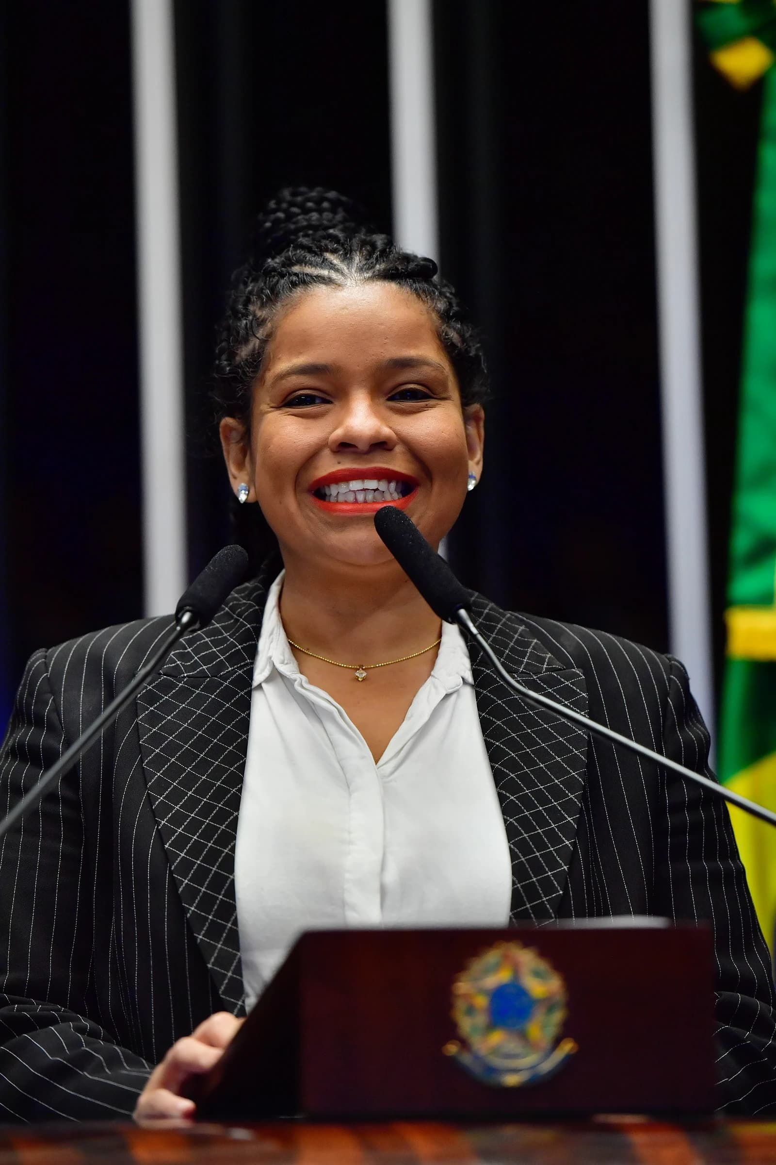 Woman with braided hair speaking at a podium in a formal setting.