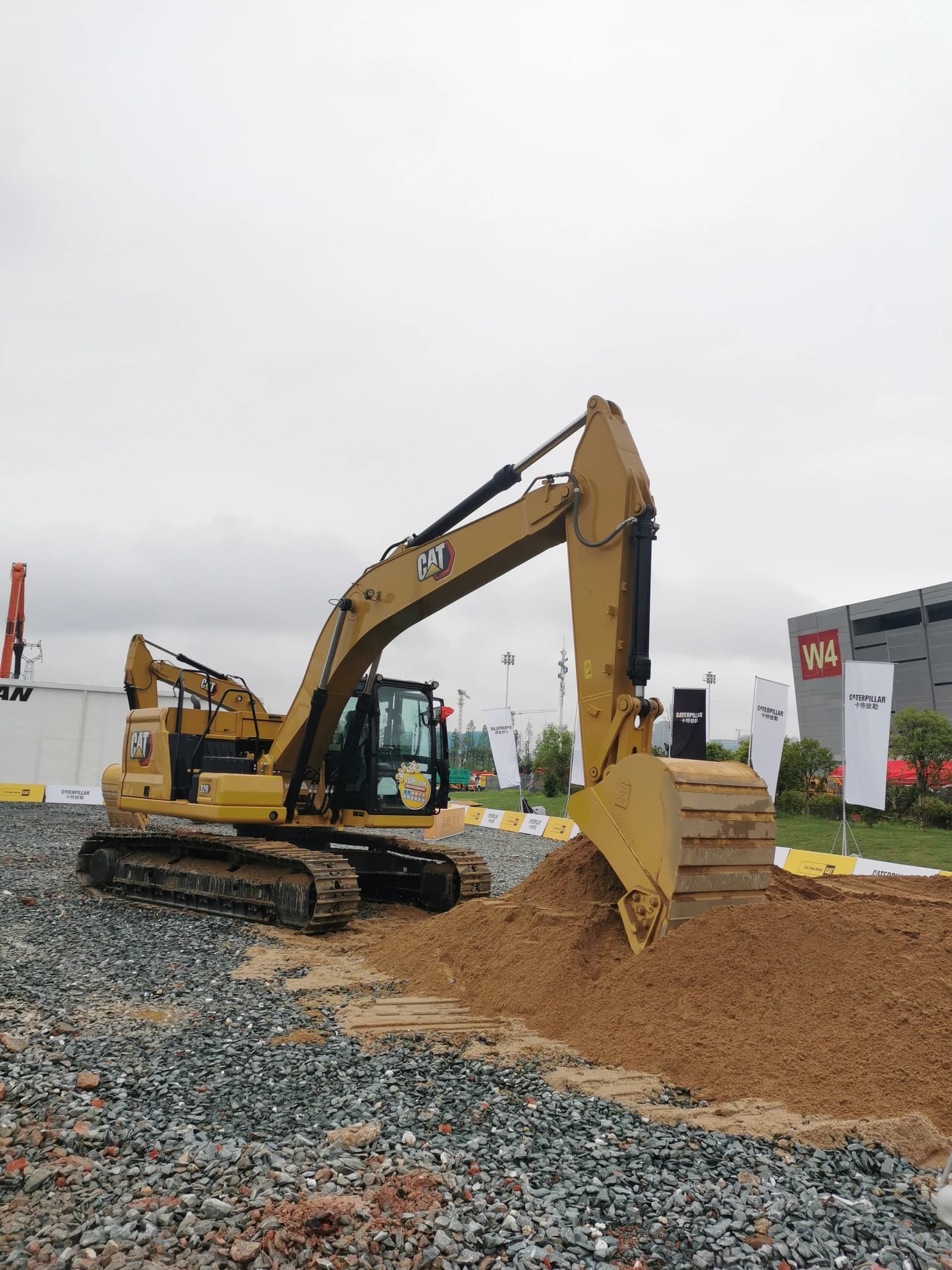 Caterpillar excavator, yellow, parked on gravel next to a pile of sand.
