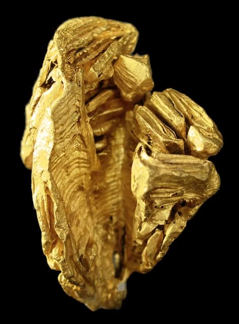 Close-up of a large gold nugget with textured surfaces on a black background.