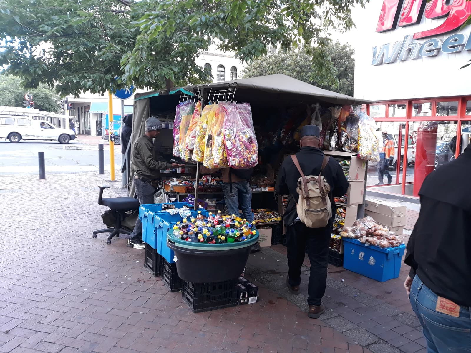 A street snack vendor serves customers from a stall on a brick sidewalk.