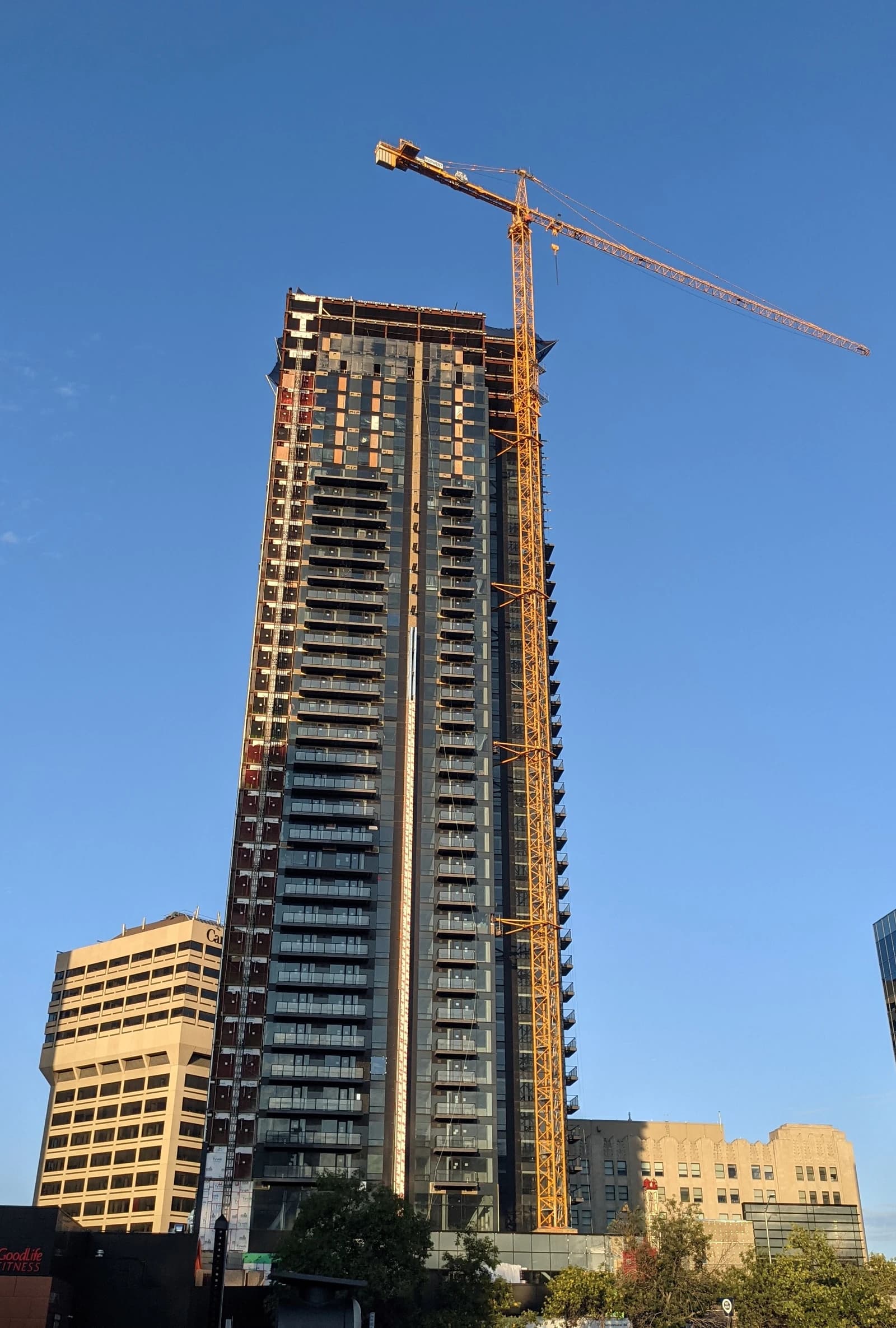 A modern high-rise building under construction with a large crane beside it.