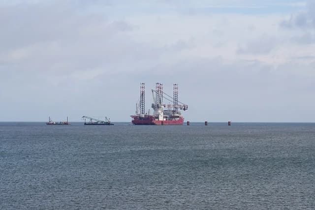 LNG Terminal Wilhelmshaven construction site featuring a large jack-up rig and smaller support boats on the water.
