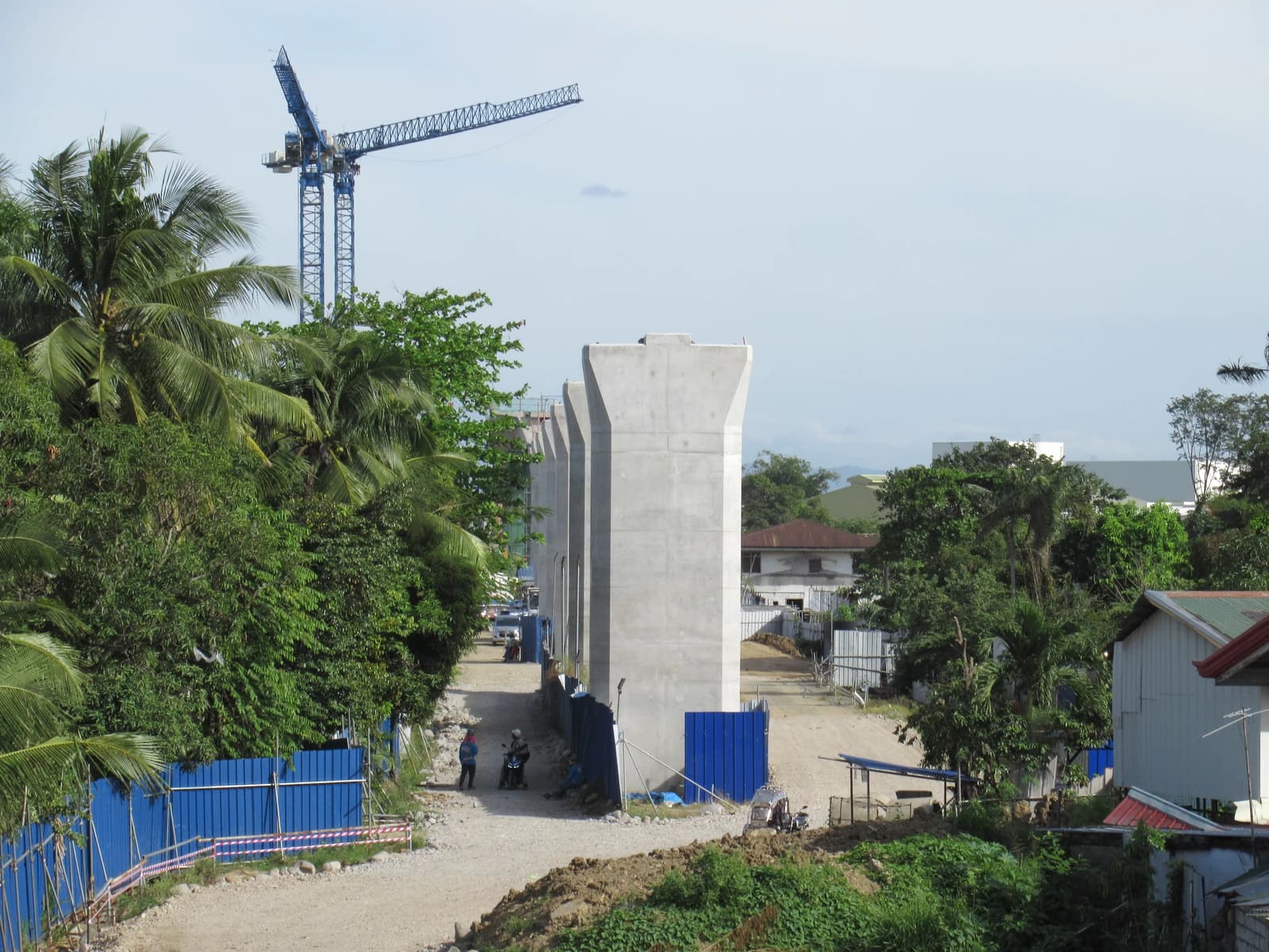Construction site with concrete bridge piers and a large blue crane in the background.