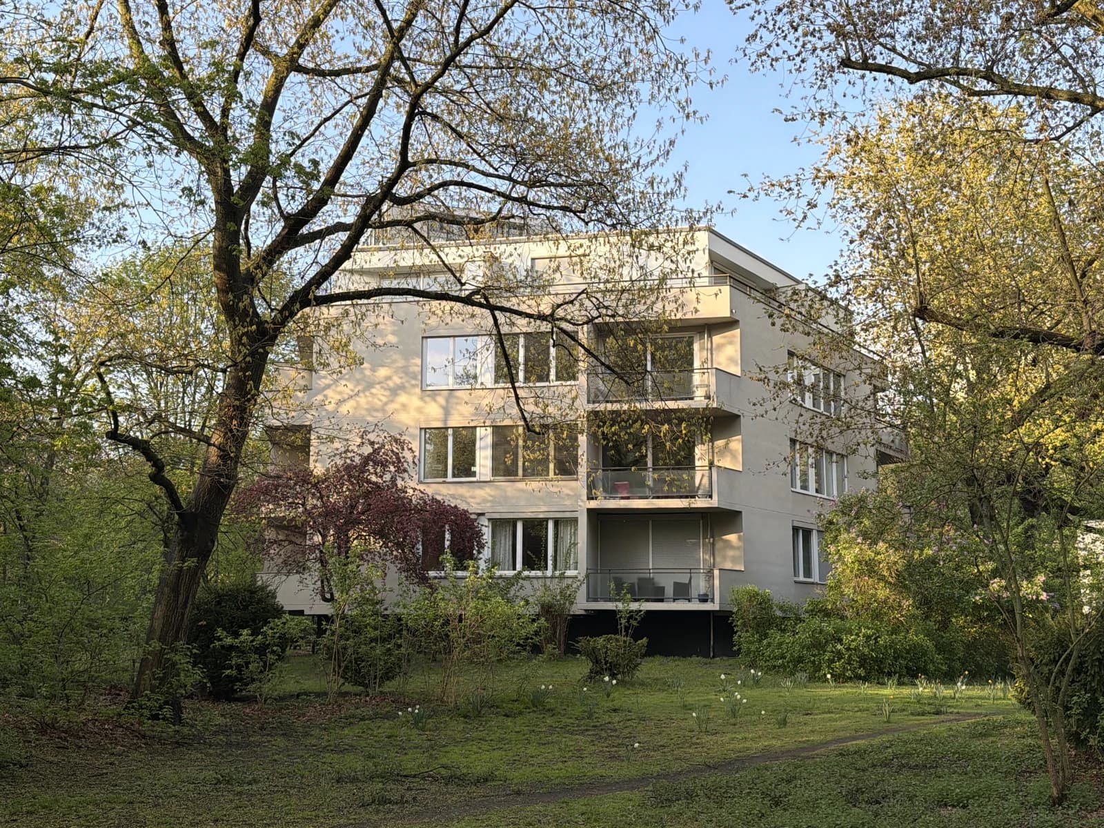 Modern residential building with balconies surrounded by lush green trees and grass.
