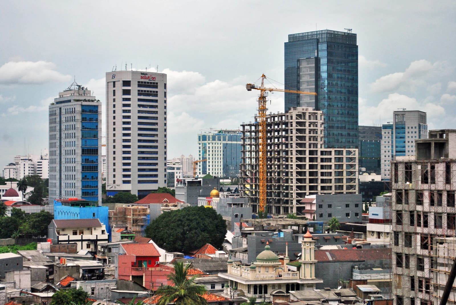 Skyline of Jakarta, Indonesia, with modern buildings and residential areas under cloudy sky.