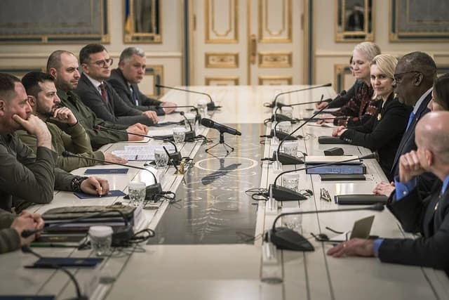 Lloyd Austin and Volodymyr Zelenskyy seated at a long table during a meeting.