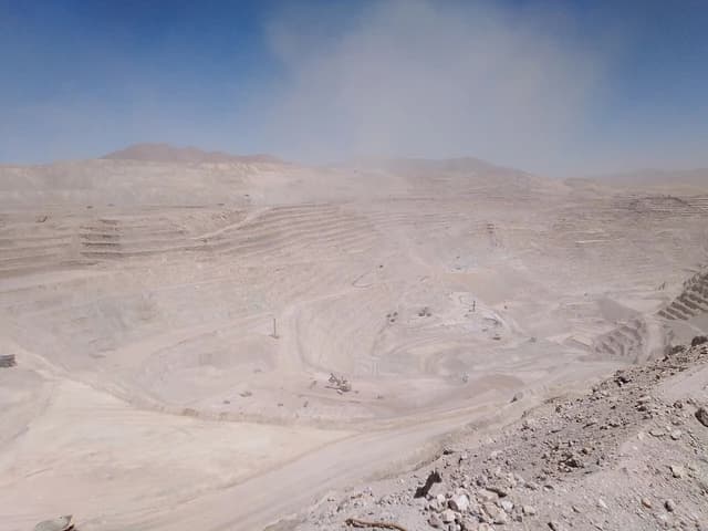 Aerial view of a large open-pit copper mine with excavators and haul trucks.