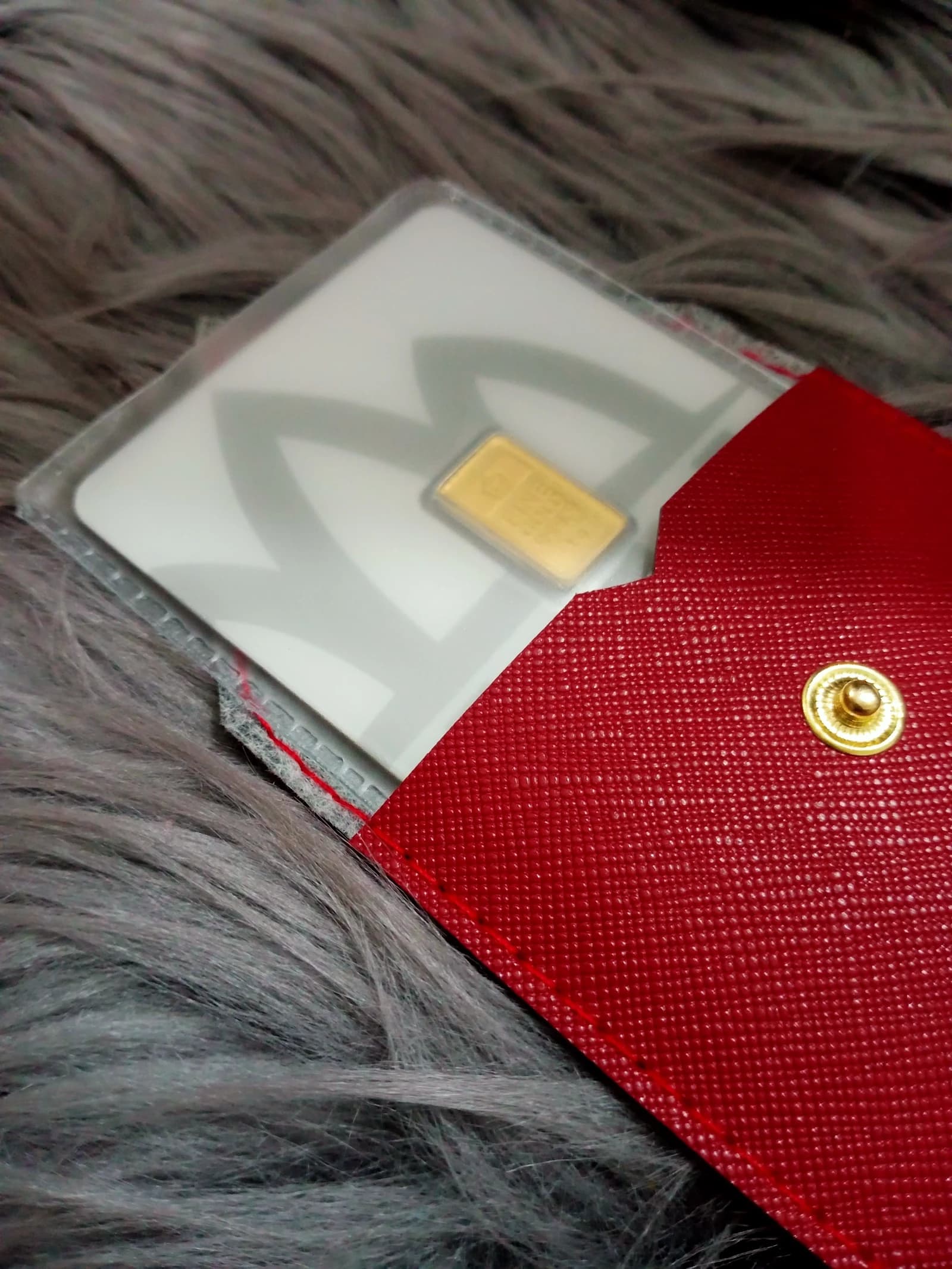 Small rectangular gold bar in a clear plastic case, partially inside a red leather wallet.
