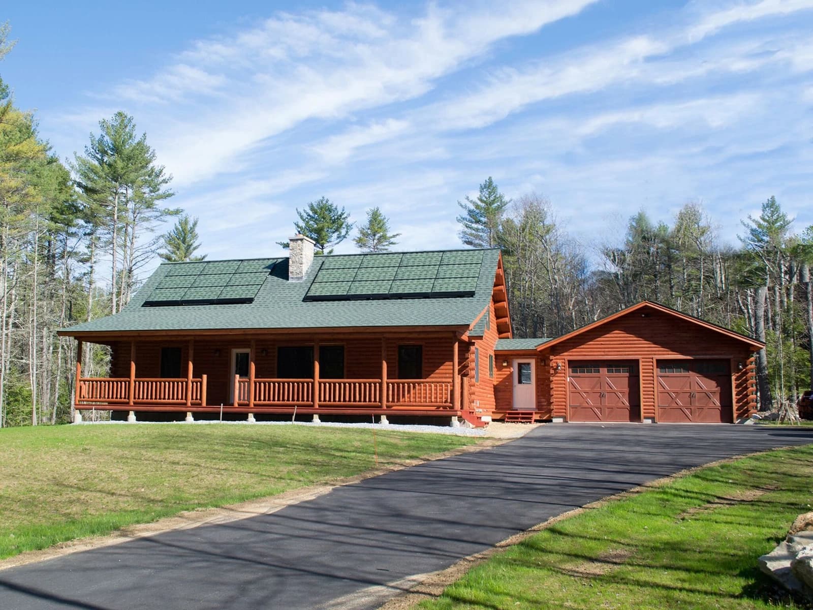 Log cabin house with green roof and solar panels, alongside an attached garage.