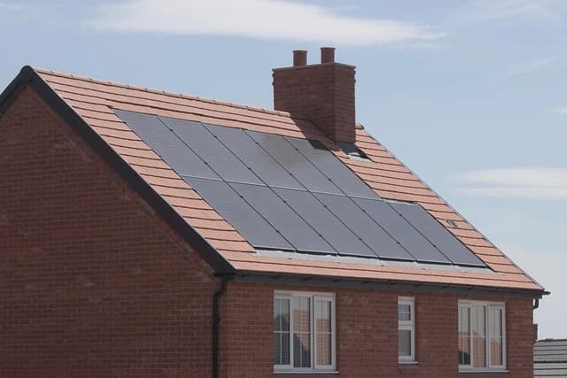 Solar panels on the tiled roof of a brick house with a chimney against a blue sky.