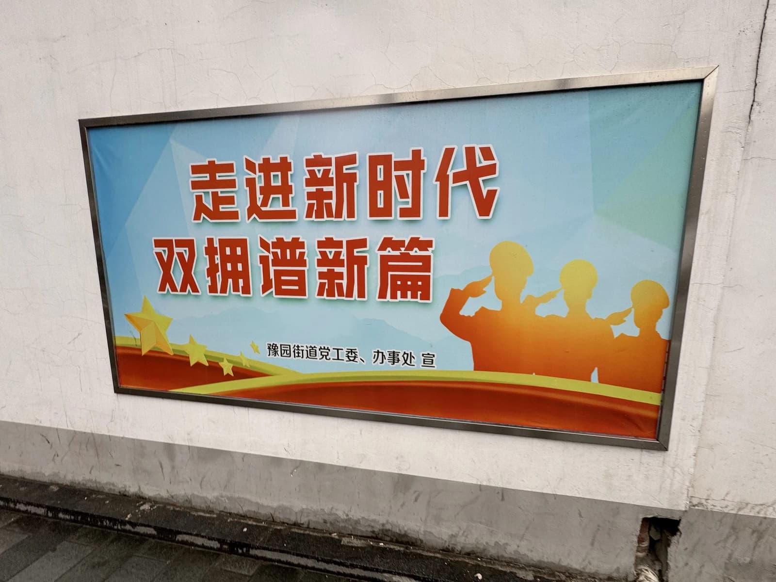 Chinese propaganda poster displayed on a wall, showing text and saluting silhouettes.