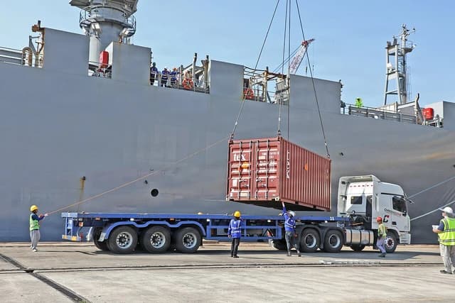 Workers loading a shipping container from a large vessel onto a truck at a port.