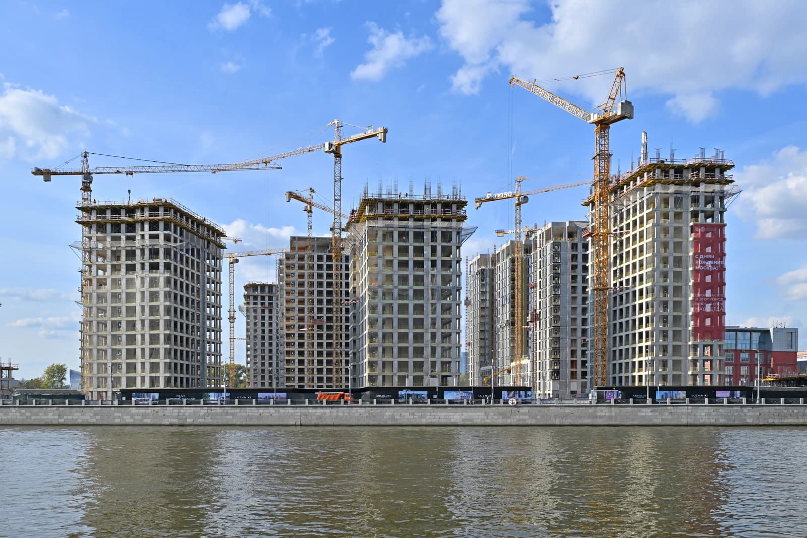 Construction cranes and unfinished residential buildings along a river in Moscow.
