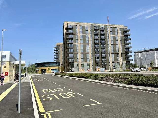 Modern apartment buildings with balconies line a street with a bus stop marking.
