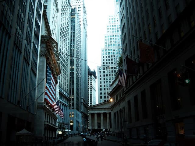 View looking down Wall Street towards the New York Stock Exchange building, with American flags.