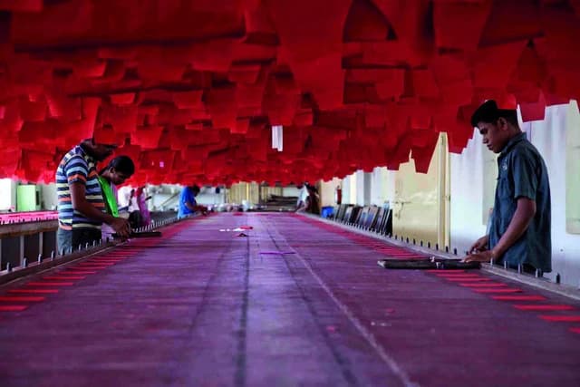 Textile workers print fabric at long tables in a factory.