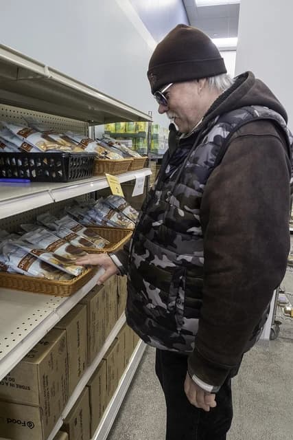 Man in a beanie and camouflage vest examining food items on a store shelf.