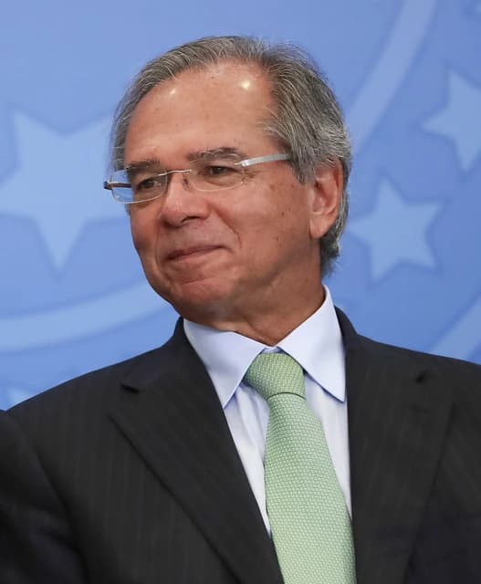 Paulo Guedes, Brazilian Minister of Economy, looking to the left and smiling.