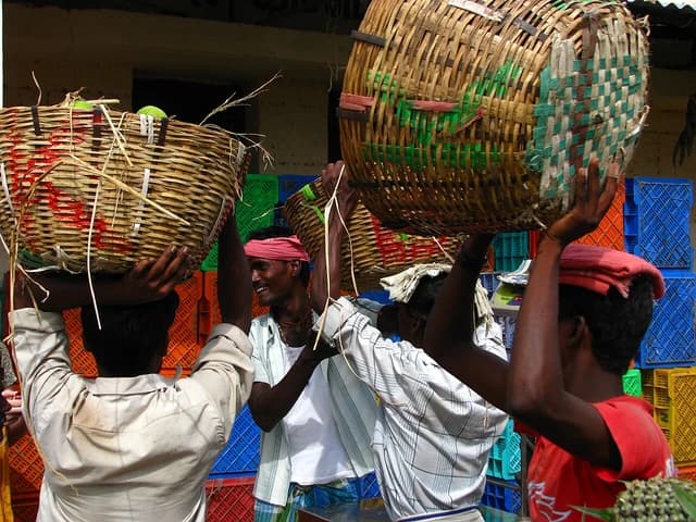 Men carrying large woven baskets on their heads in a market setting.
