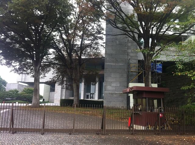 Exterior of the Supreme Court building in Tokyo, seen through a gate with trees.