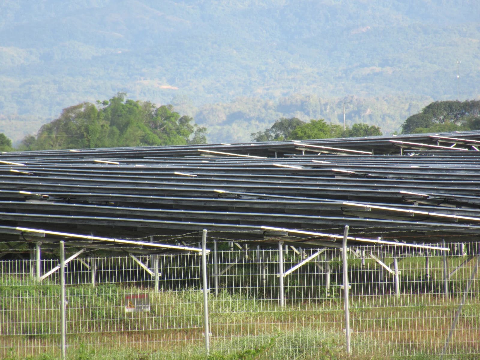 Rows of solar panels behind a fence at a renewable energy facility.