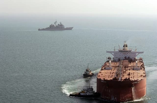 US Navy guided missile cruiser USS Mobile Bay patrols near a super oil tanker.