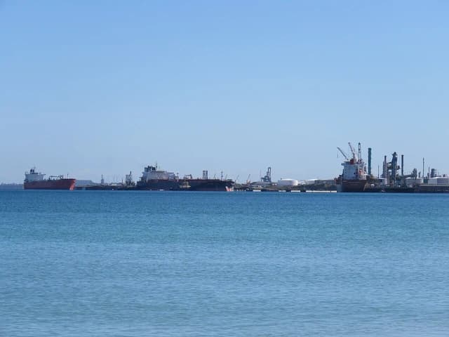 Oil and chemical tankers docked at an oil refinery jetty with industrial structures in the background.