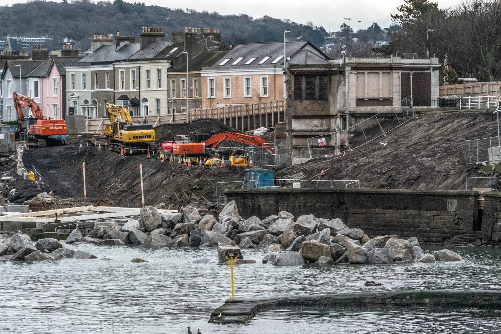 Construction site on waterfront with buildings in background.