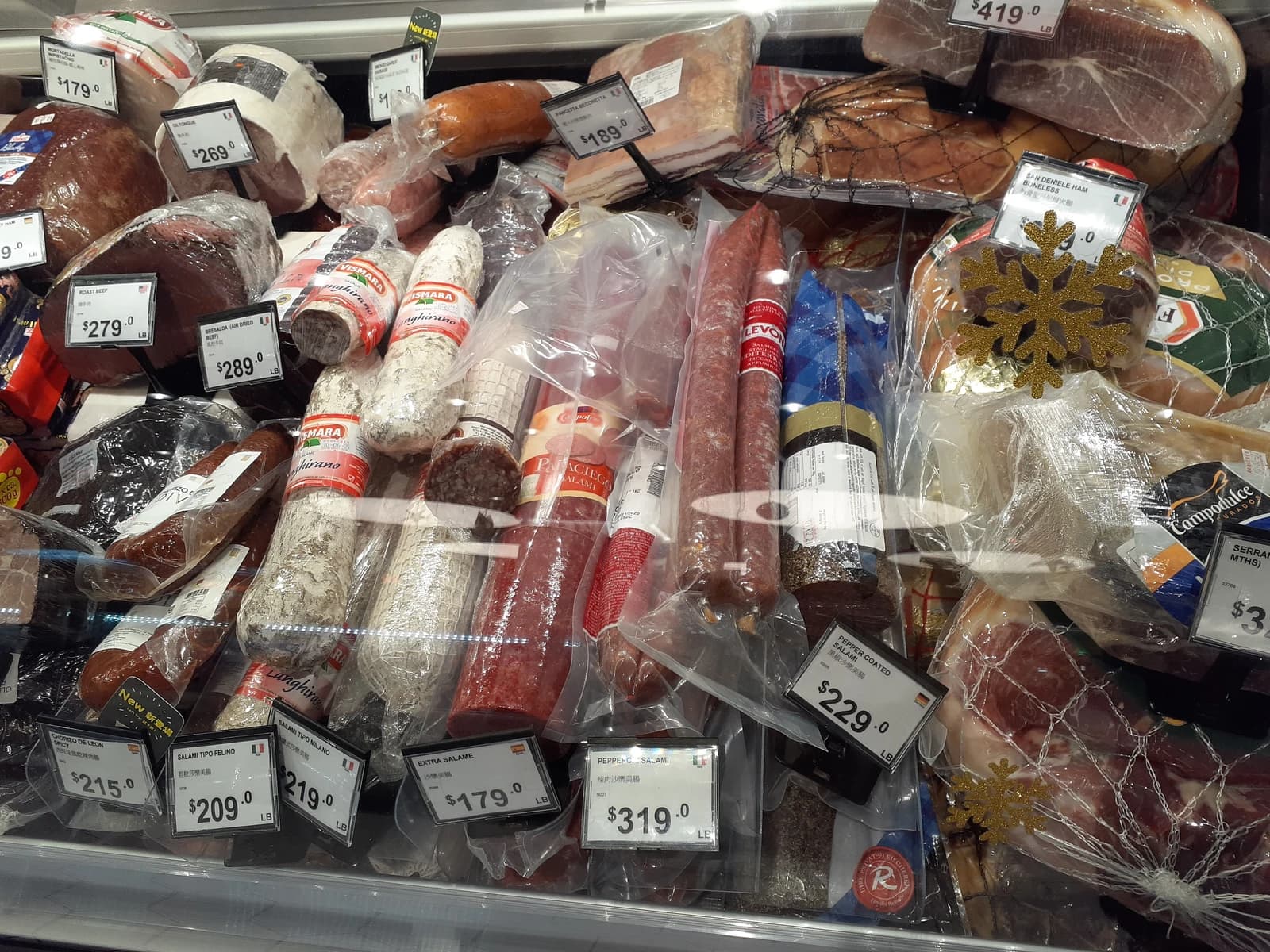Packaged meat products, including salamis and hams, are displayed with price tags in a supermarket.