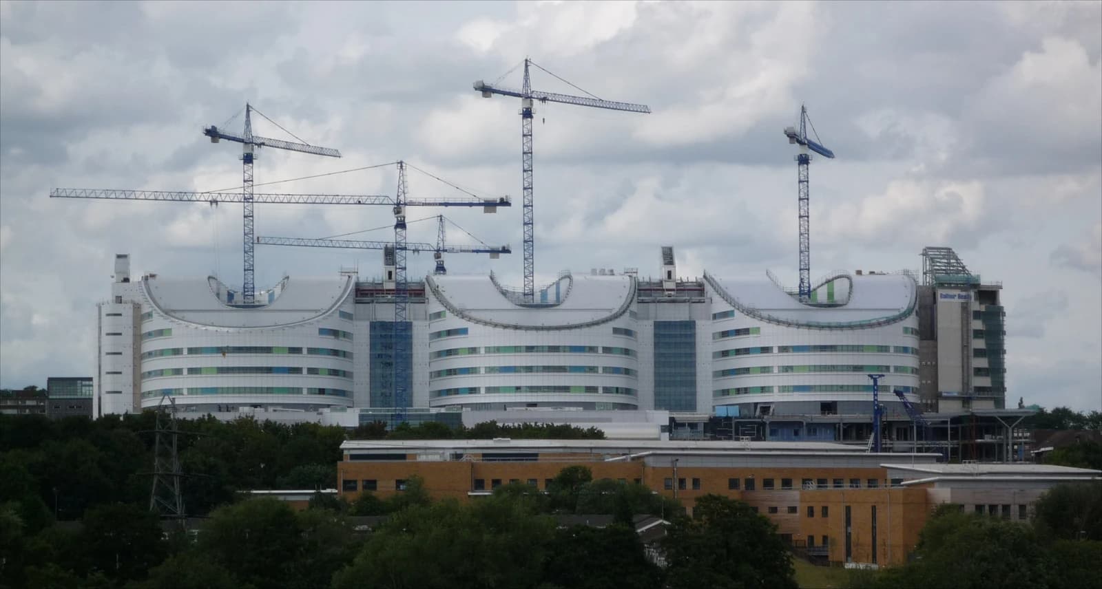 Large hospital building under construction with several tall cranes visible above it.