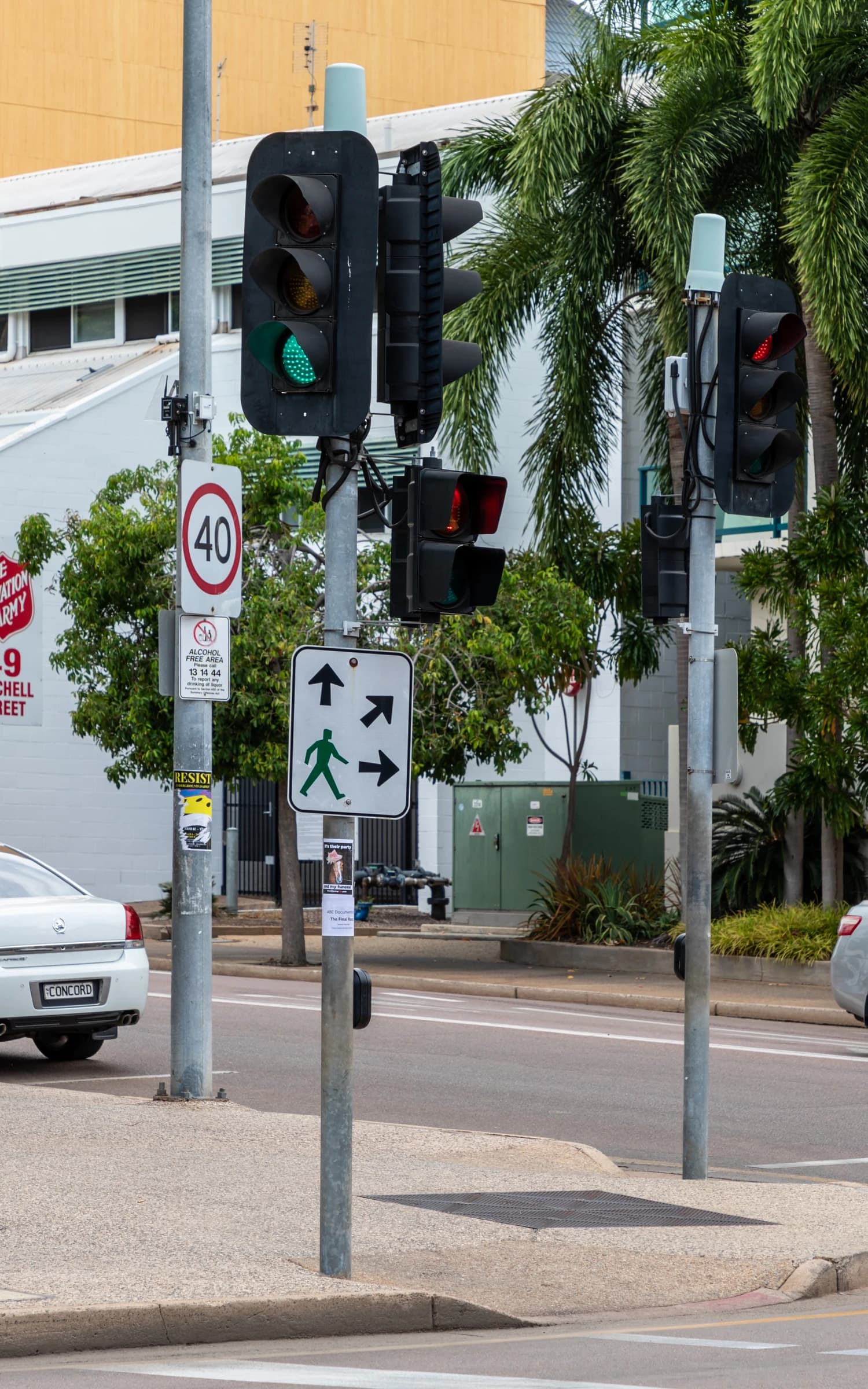 Traffic lights with green signal for vehicles and pedestrian crossing signs on poles at a city intersection.