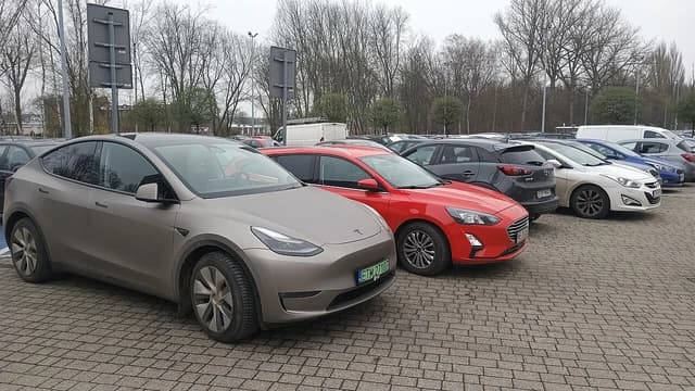 Gray Tesla Model Y electric car with Polish license plates parked in an outdoor lot.