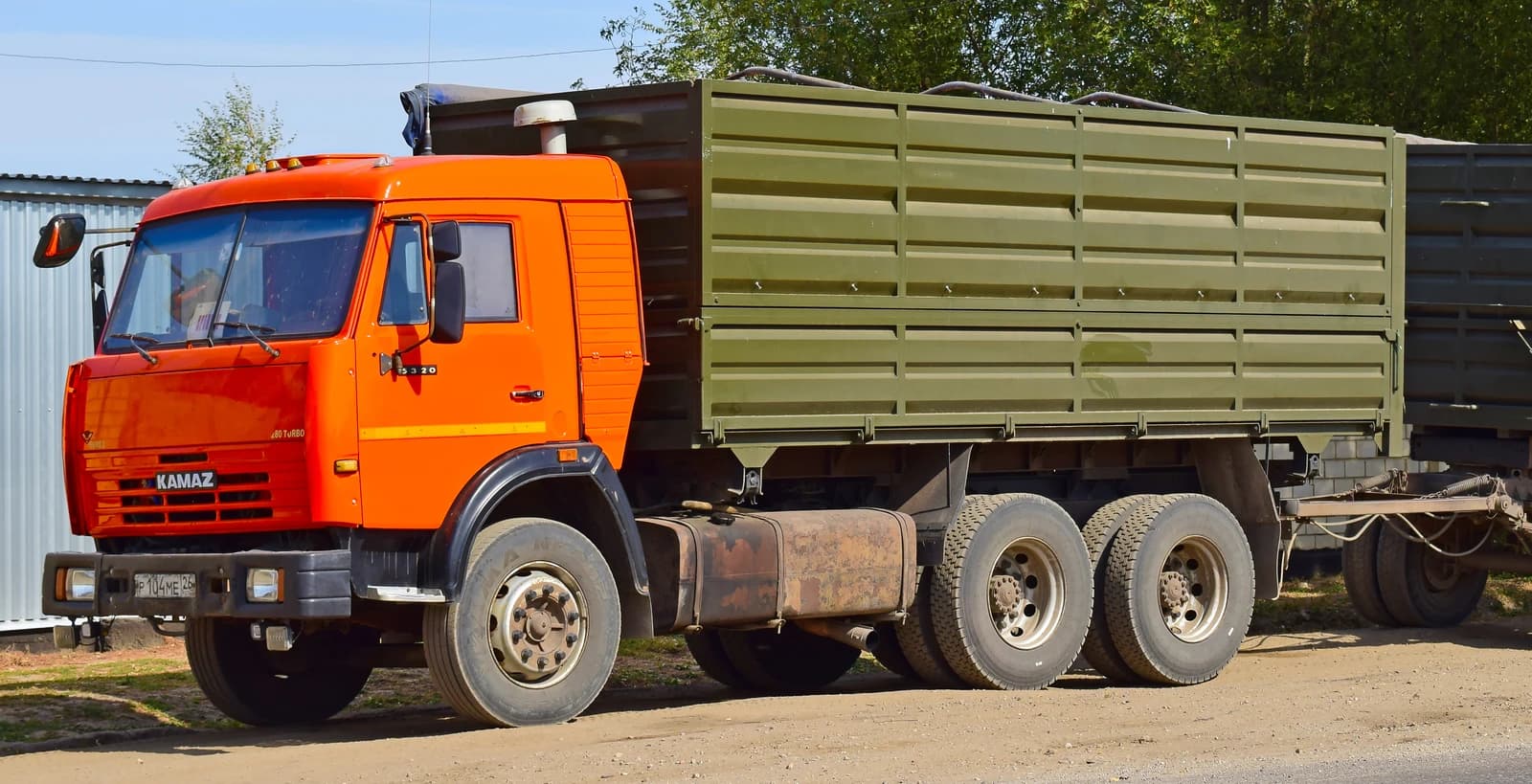 An orange Kamaz truck with a green cargo bed parked on a dirt road.