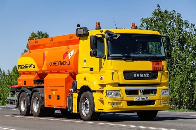 A yellow and orange KAMAZ-65207-based fuel tank truck drives down a road.