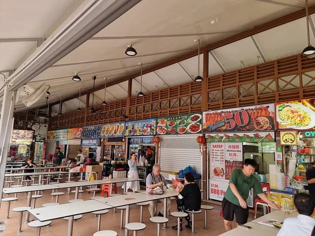 People sitting at tables in an outdoor food hawker center in Singapore.