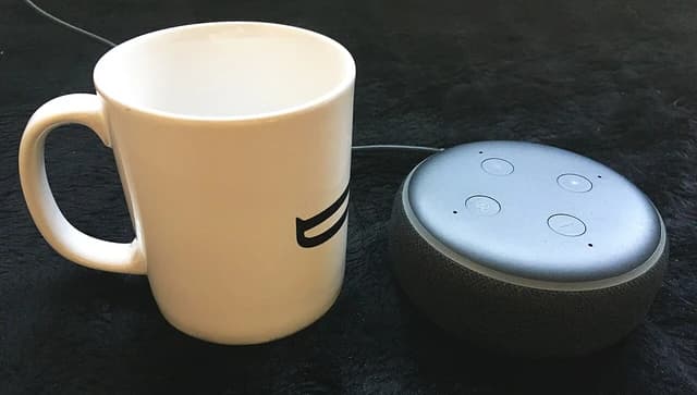 Amazon Echo Dot smart speaker displayed next to a white ceramic coffee mug.