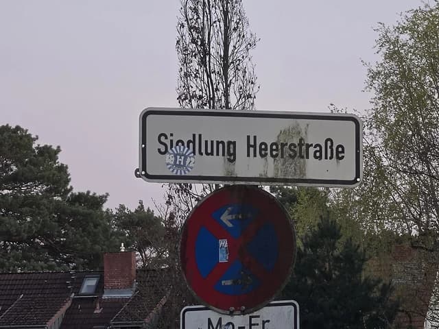 Street sign displaying 'Siedlung Heerstraße' with trees in the background.