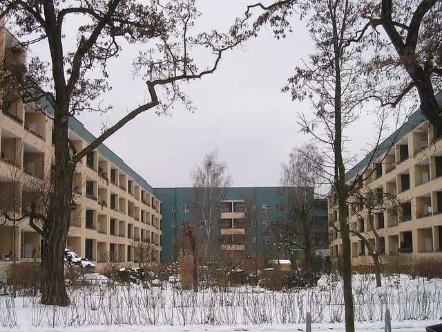 Apartment buildings with multiple floors and balconies enclose a central green space covered in snow.