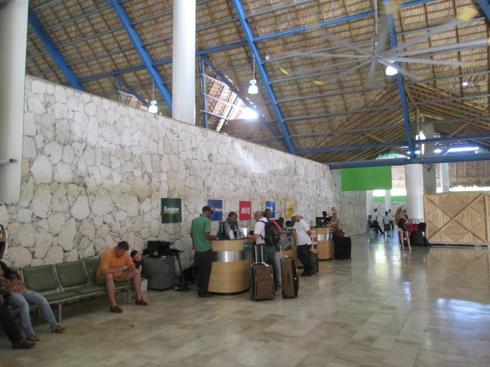 Travelers stand at rental car counters from various companies in an airport terminal.