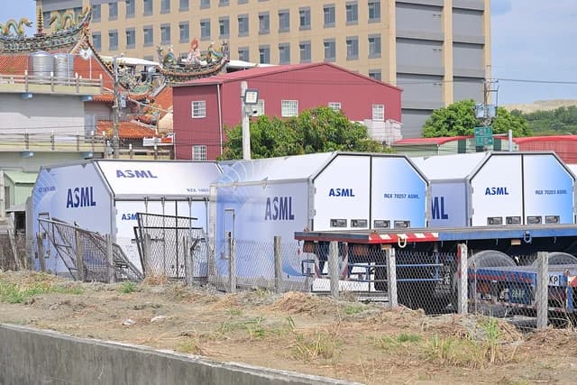 ASML air freight containers with blue and white branding on trucks in an industrial area.