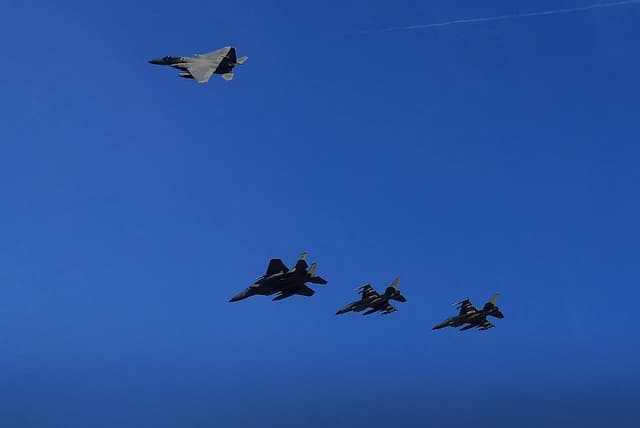 Four fighter jets, an F-15C Eagle and three F-16s, fly in formation against a clear blue sky.