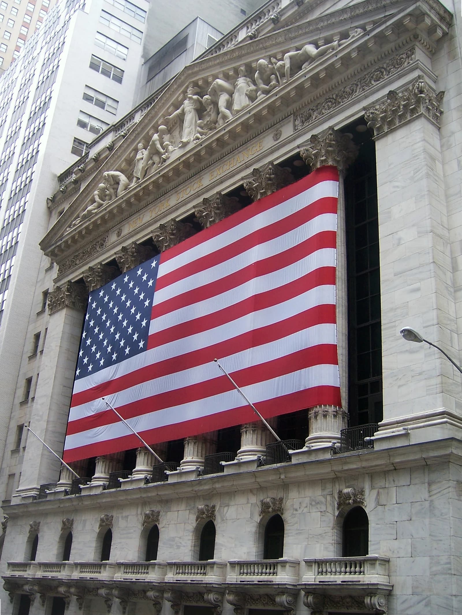 Neo-classical facade of the New York Stock Exchange building displaying a large American flag.