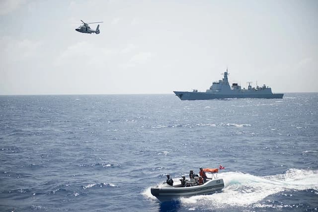 Chinese destroyer Xi'an (DDG 153) sails with a helicopter overhead and a small boat nearby.
