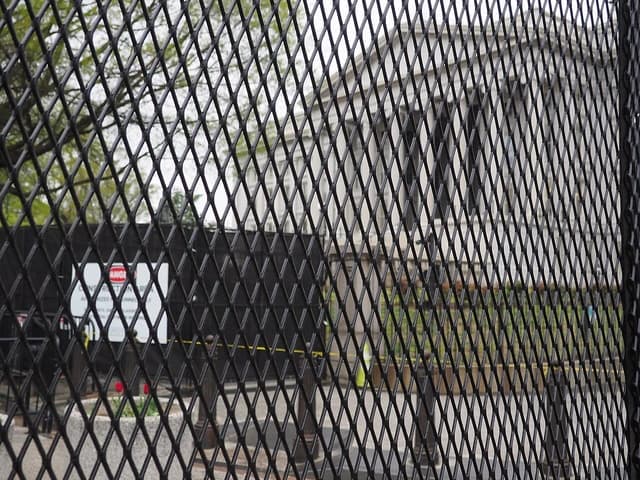 U.S. Treasury Building seen through a metal security fence from a distance.