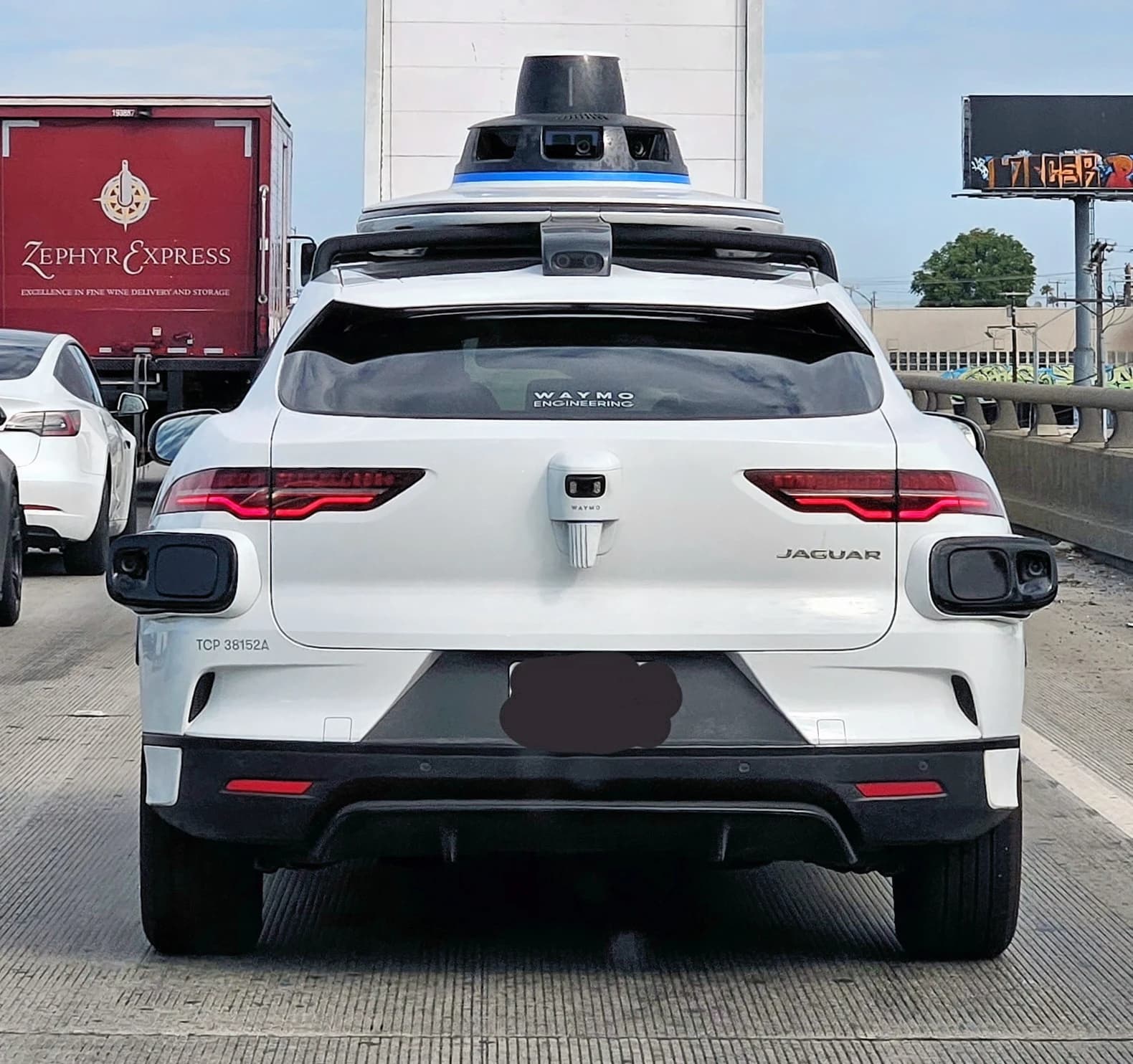 A white Waymo self-driving car with sensors visible, driving on a freeway.