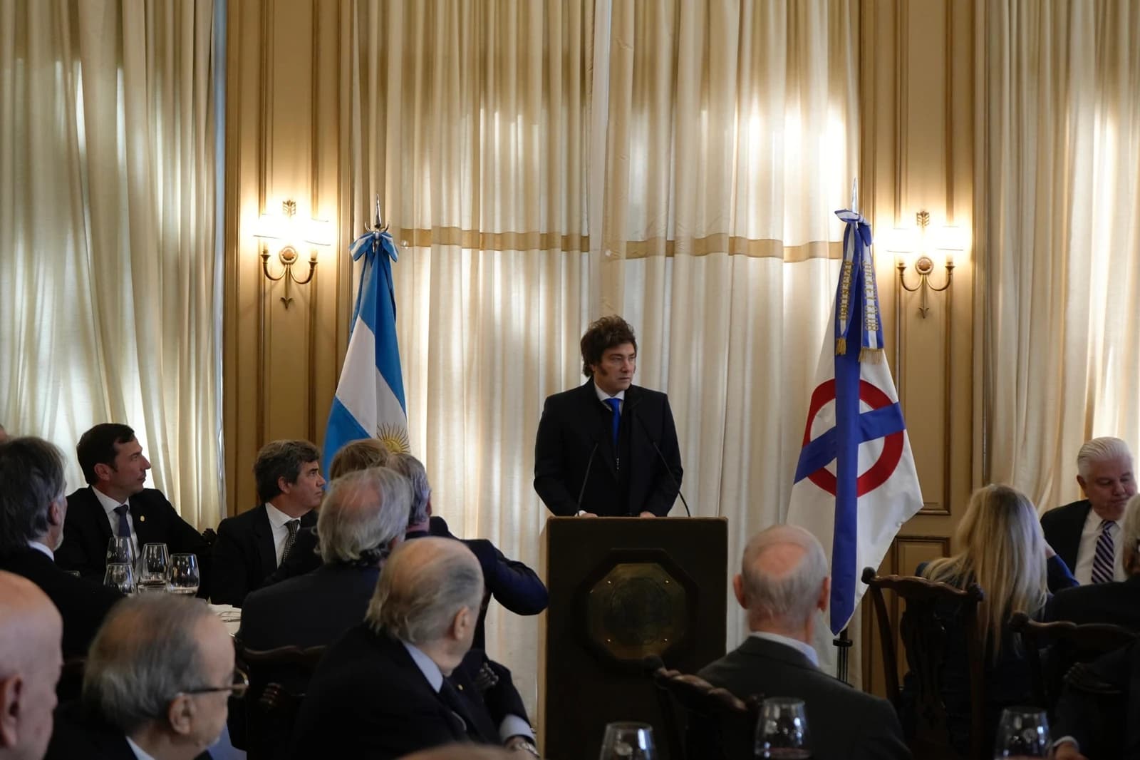 Argentina President Javier Milei speaks at a podium to an audience in a formal room.